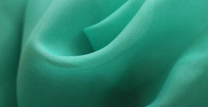 A close-up view of smooth green polyester fabric with soft folds and gentle sheen.