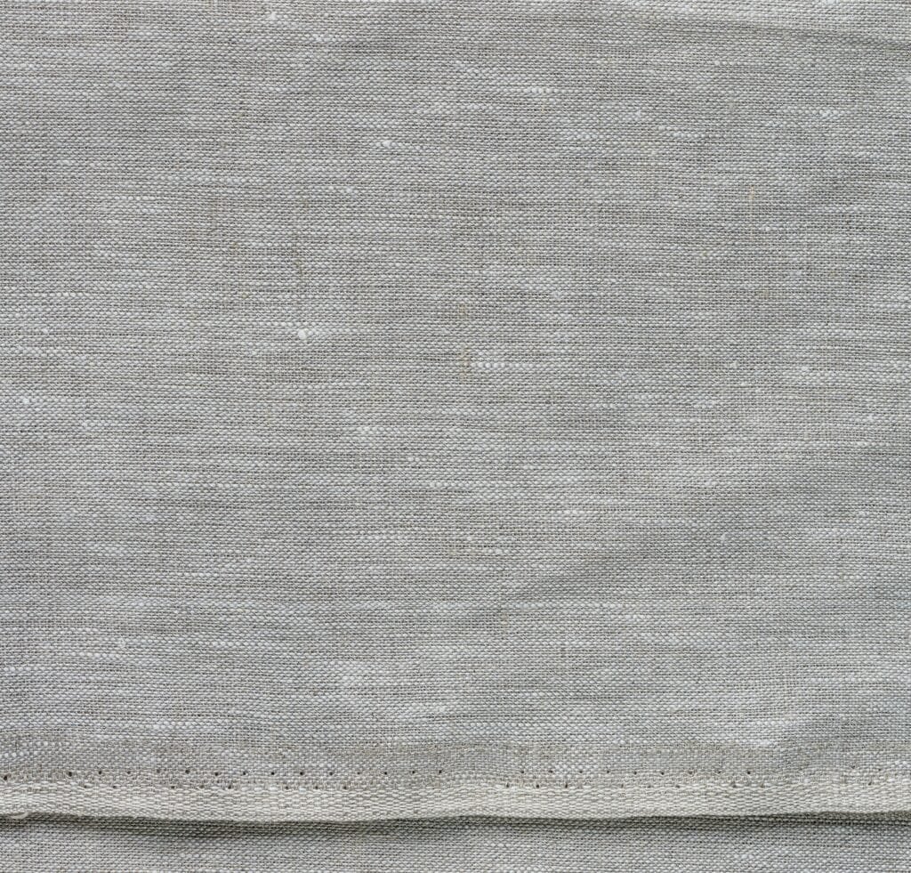 “Close-up view of gray crash linen fabric with a soft, textured weave and a folded hem along the bottom edge.”