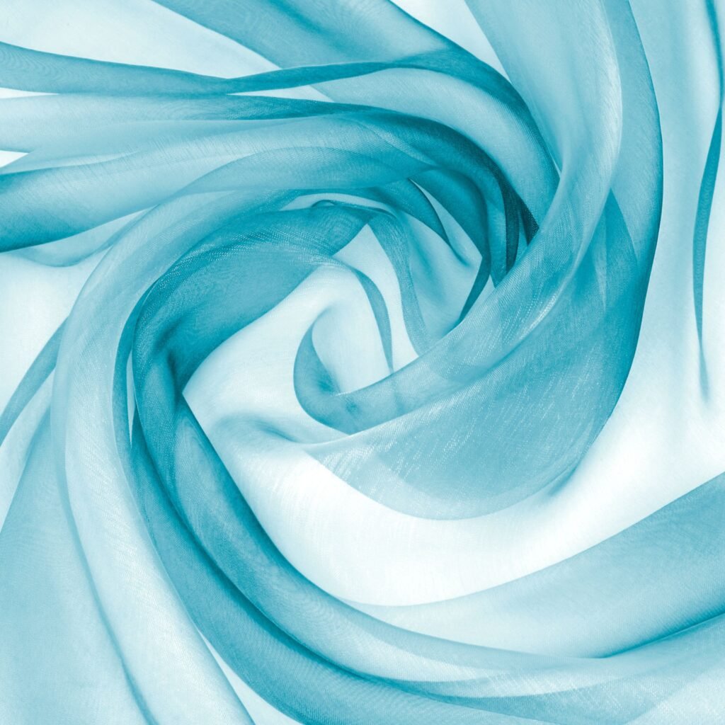 A close-up image of crystal organza fabric in light blue, showing sheer, flowing layers that gleam and reflect light as they swirl into soft folds.