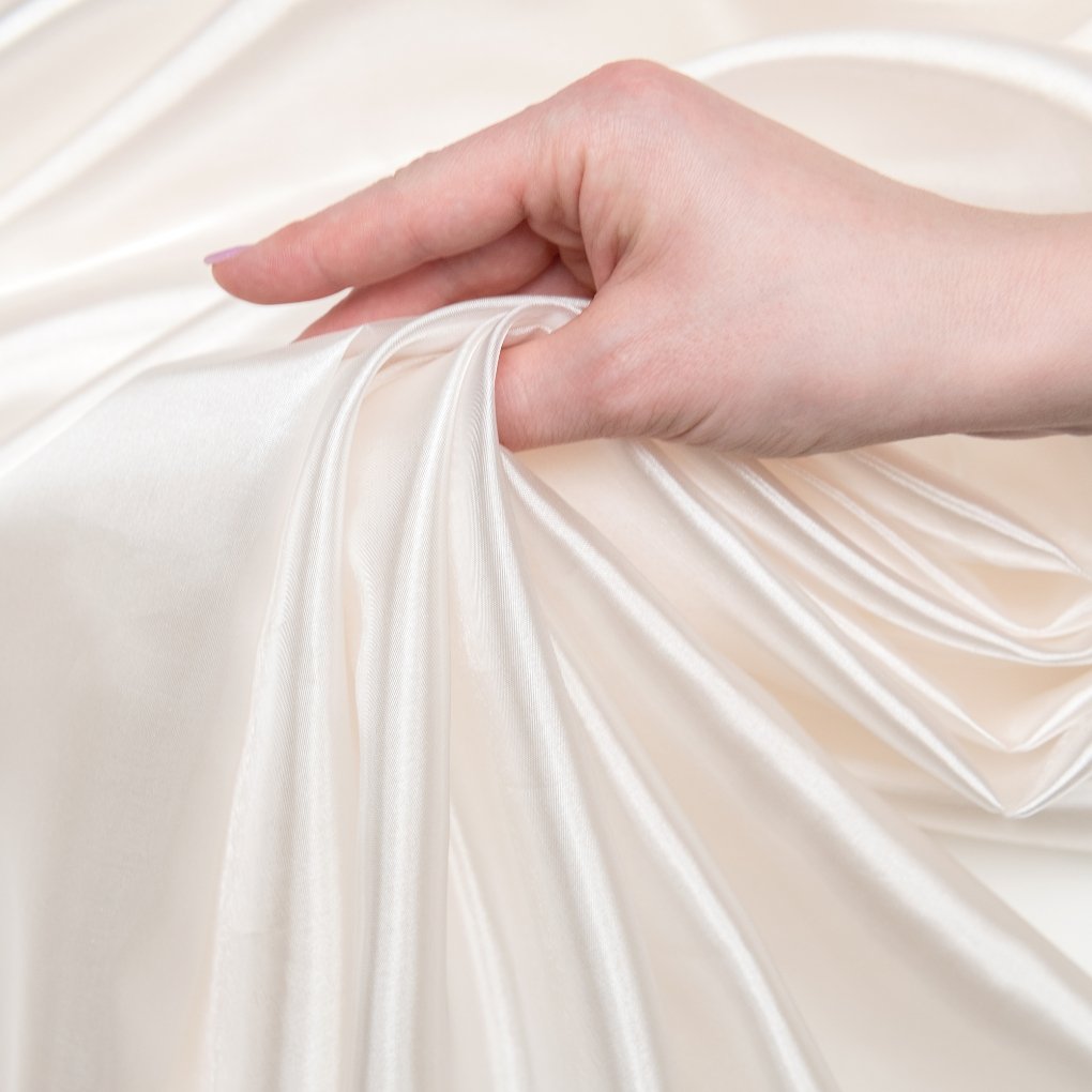 A close-up of a hand gently gathering sheer, crystal-clear organza fabric with a lustrous, glassy sheen and smooth folds.