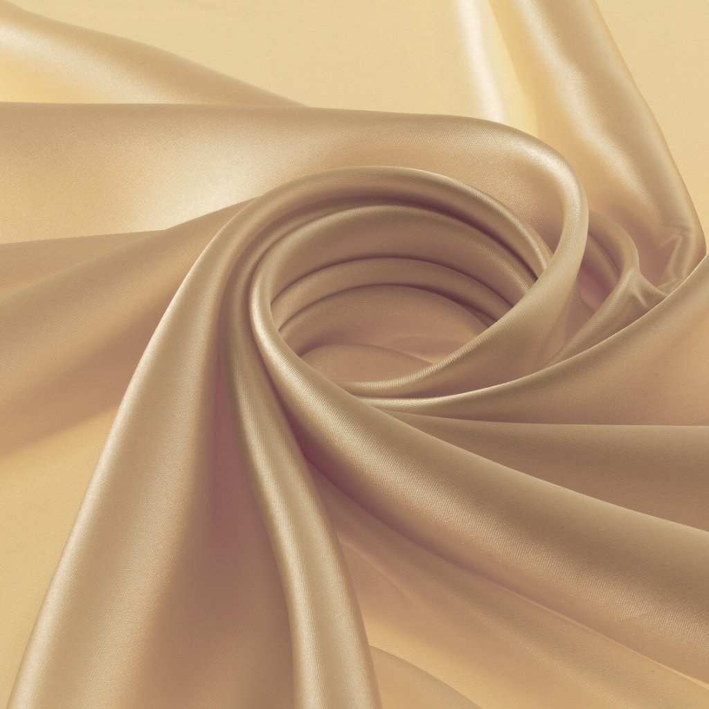 A close-up of luxurious satin organza fabric in soft champagne tones, draped and twisted to showcase its smooth sheen and flowing folds.