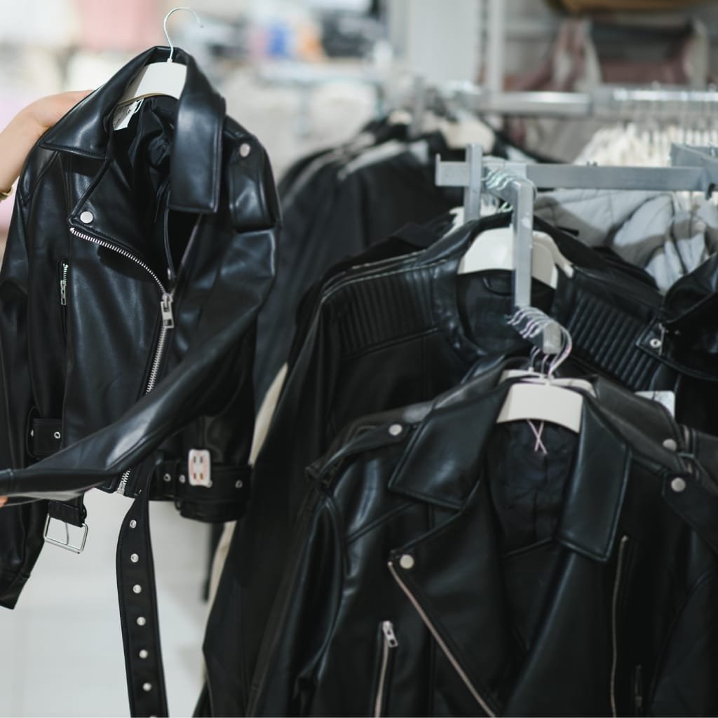 A row of black leather jackets on hangers in a clothing store, with one jacket being held up to view its front zipper and belt.