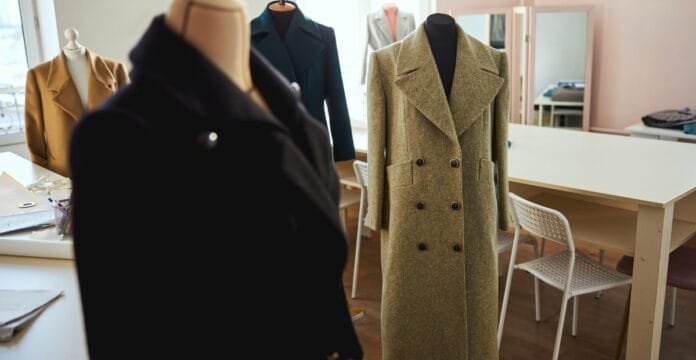 Beige double-breasted wool coat on a mannequin in a fashion studio, with other coats on display in the background