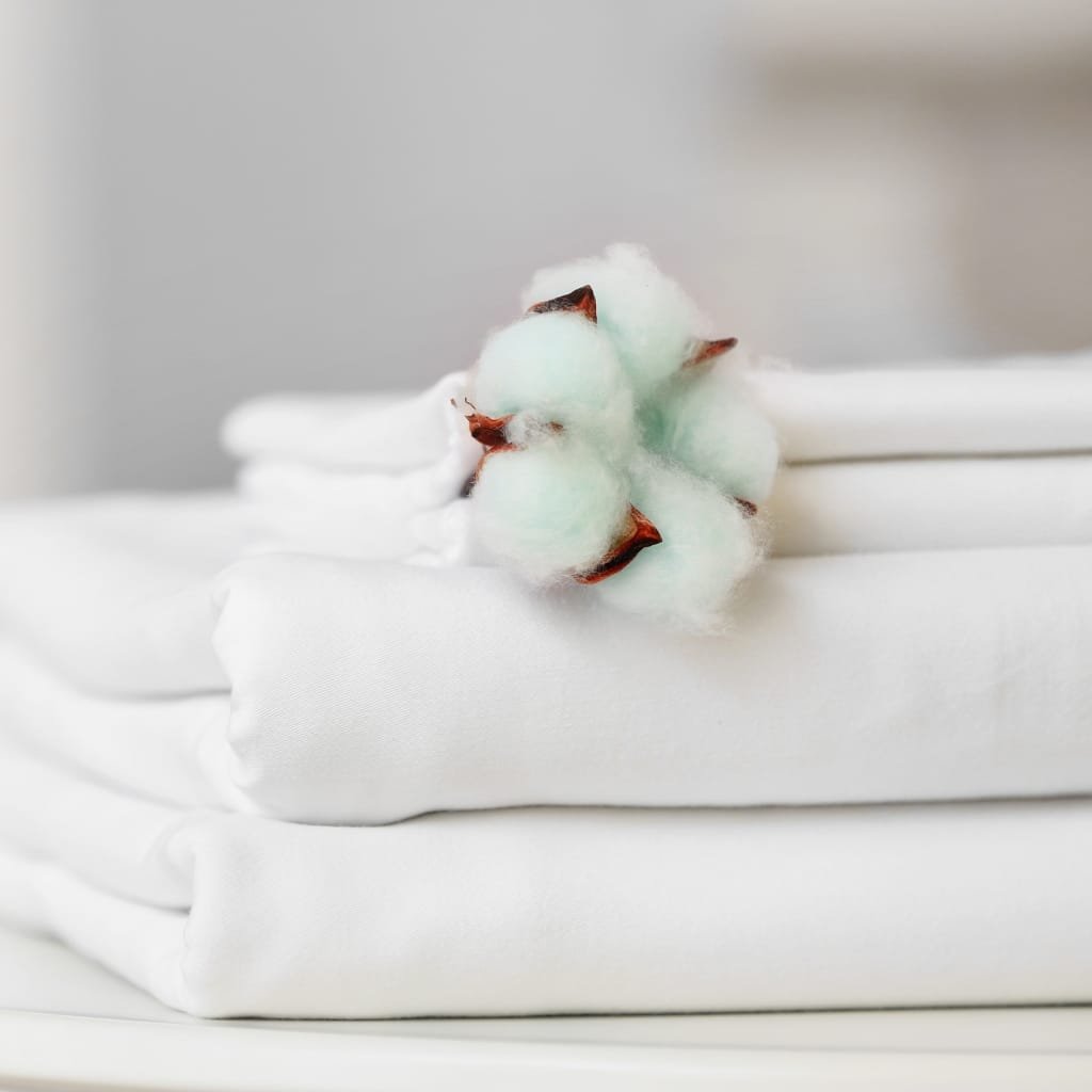 Close-up of crisp white Egyptian cotton sheets folded neatly with a soft cotton boll resting on top, highlighting durability and luxury.