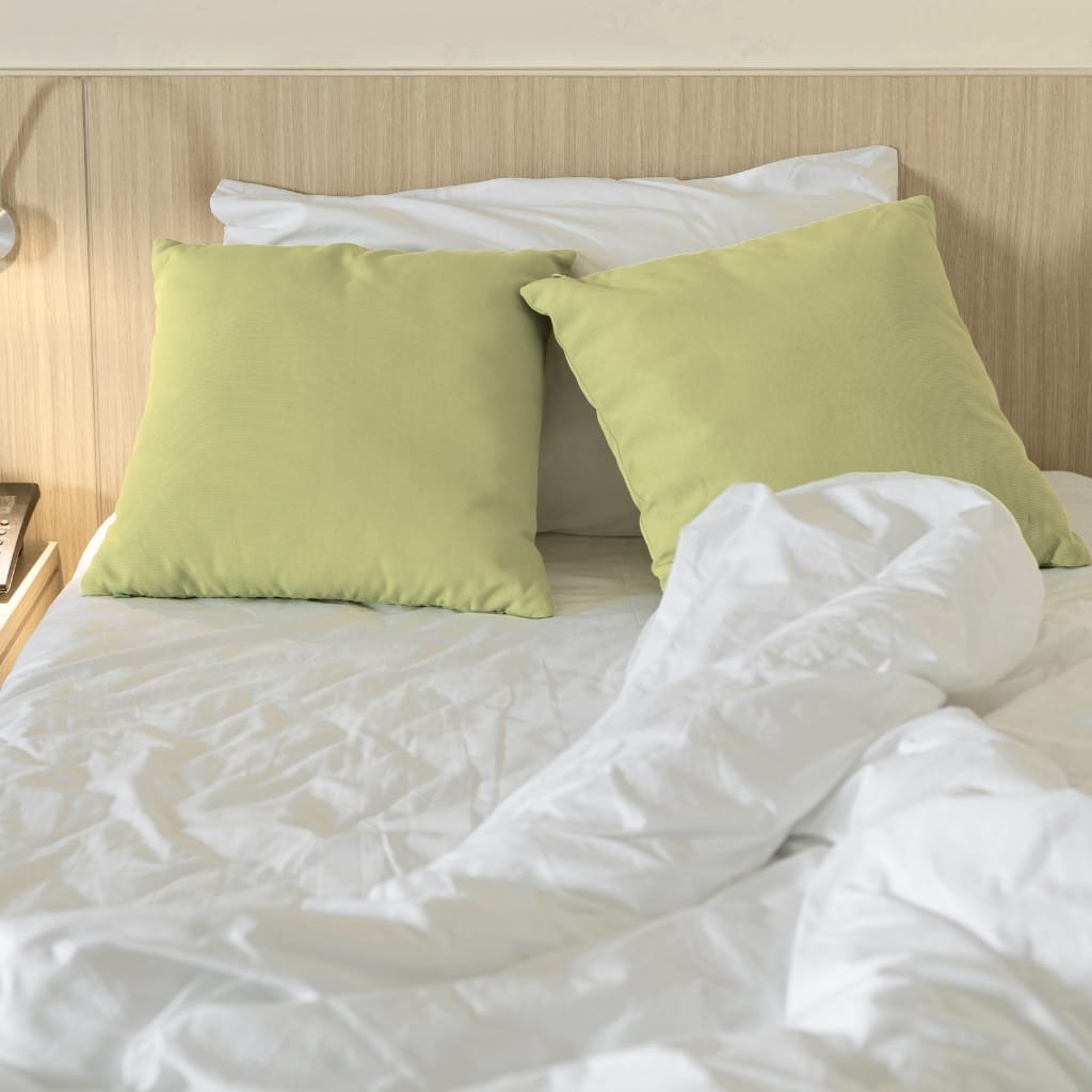 “A neatly made bed with white sheets and two light green pillows, suggesting luxurious Egyptian cotton bedding.