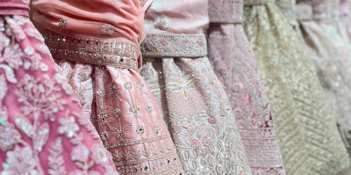 A row of pastel pink to ivory embroidered garments made from organza, each piece featuring intricate floral and geometric embroidery with shimmering bead and sequin details along the borders and bodices. Embroidered Organza Fabric