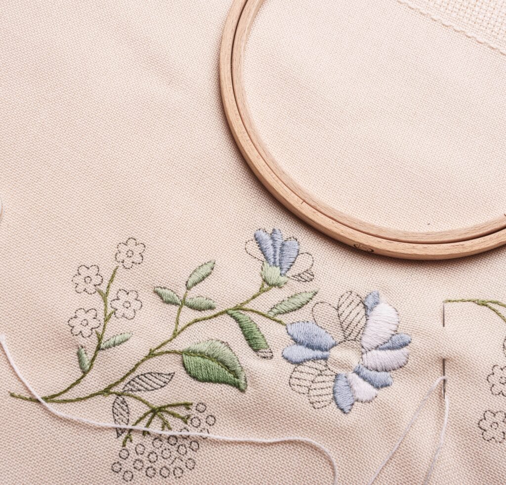 Embroidered floral design on light linen fabric with pastel blue and green threads.