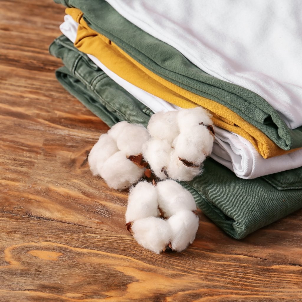 Why Supima Cotton Feels Softer, Stronger, and Smarter 20 Stack of folded clothing in green, yellow, and white tones placed on a wooden surface, with white cotton bolls resting beside the stack.
