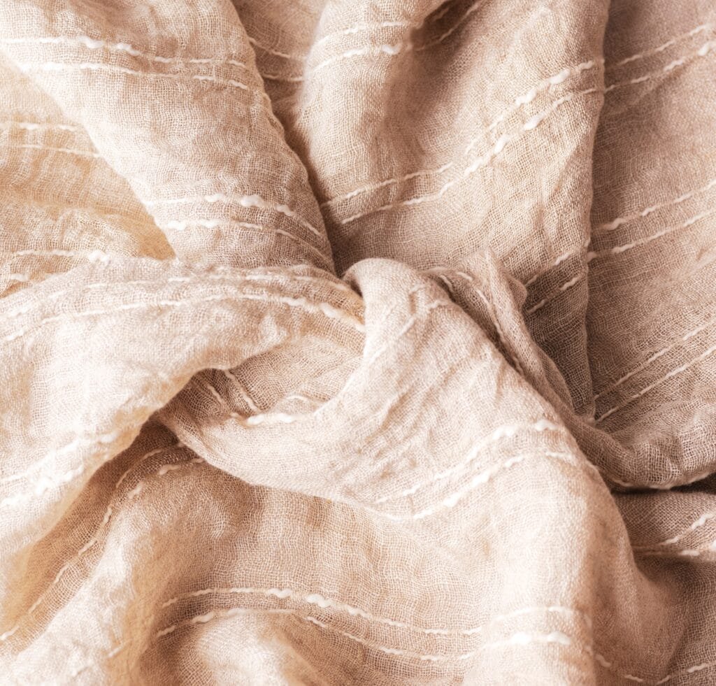 “Soft beige gauze linen fabric with subtle white stitched stripes, gently folded and knotted.”