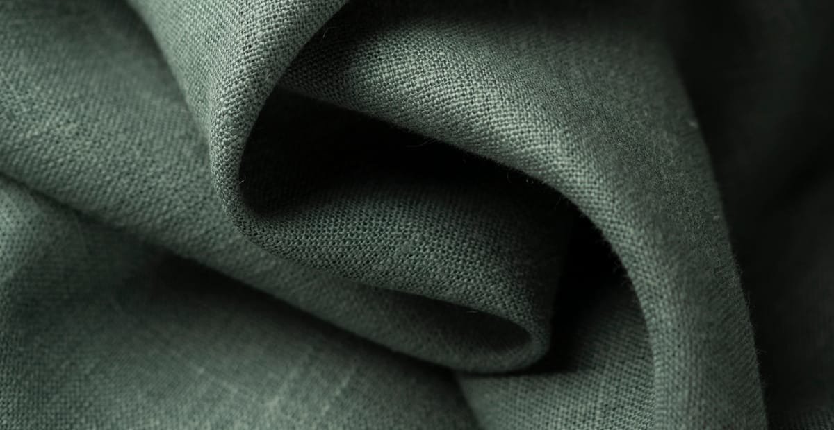 "Close-up of dark green linen fabric with soft folds and a textured weave."