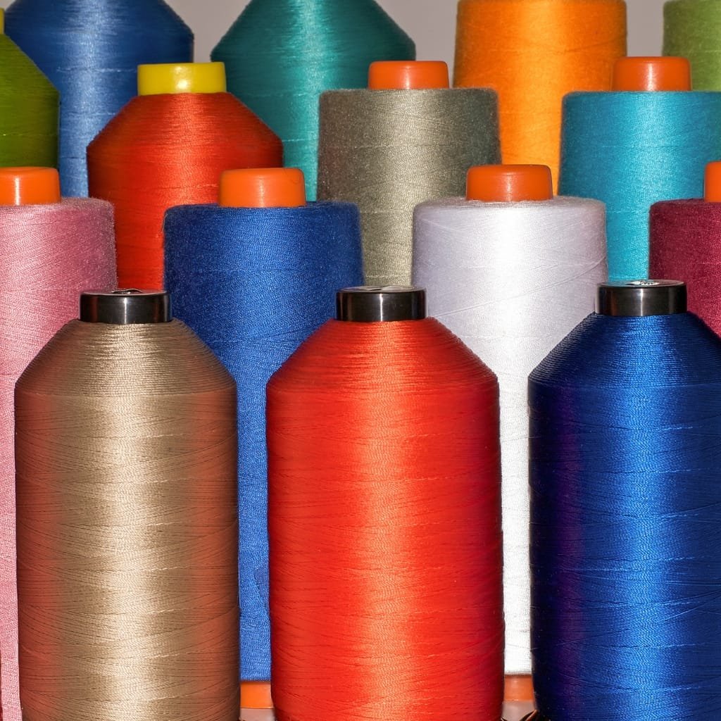 High-Tenacity Polyester: Strength, Durability & Key Benefits 5 A close-up view of numerous colorful spool threads arranged in rows, featuring high-tenacity polyester threads in shades of red, blue, brown, white, orange, and green.