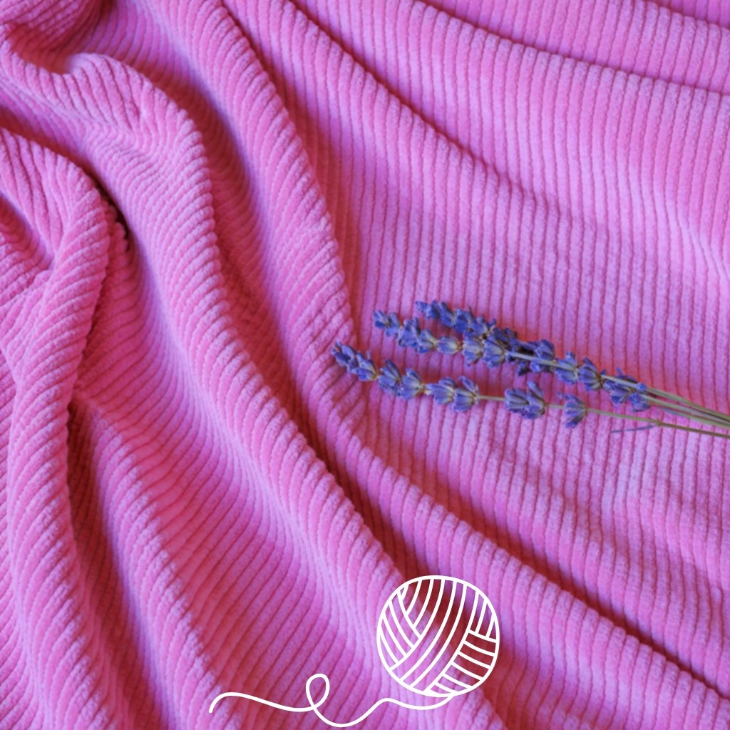 Close-up of bright pink corduroy wool fabric with its distinctive ribbed texture, featuring a small cluster of purple lavender stems placed on it.