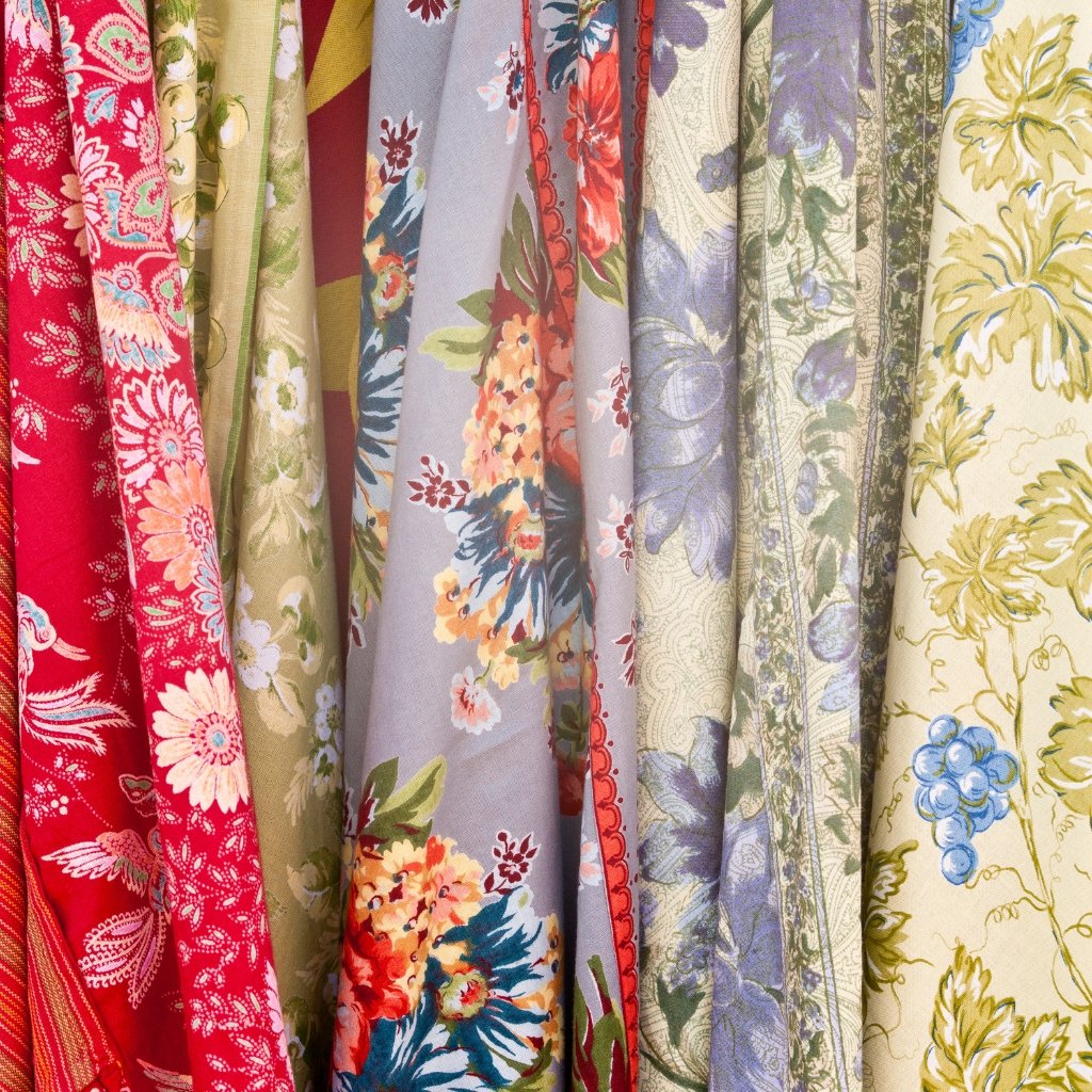 Close-up of printed organza fabric with vibrant floral patterns in red, pink, green, lavender, and cream colors, showing delicate, sheer texture and fine embroidery-like details.
