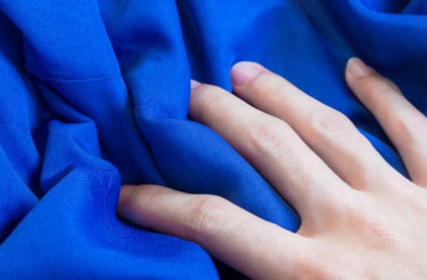 A hand touching smooth blue fabric, showing texture and softness.
