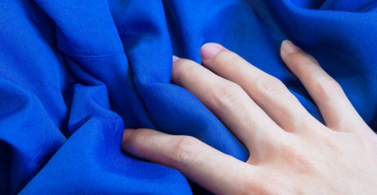 A hand touching smooth blue fabric, showing texture and softness.