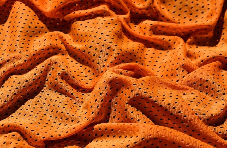 Orange perforated fabric with small black dots, draped in soft folds.