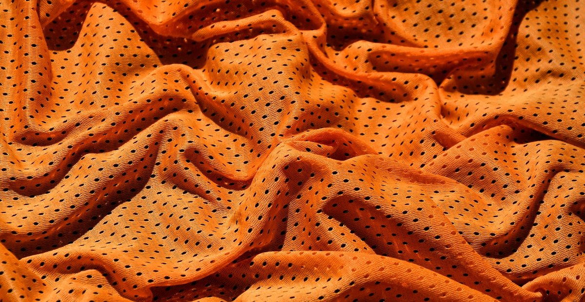 Orange perforated fabric with small black dots, draped in soft folds.