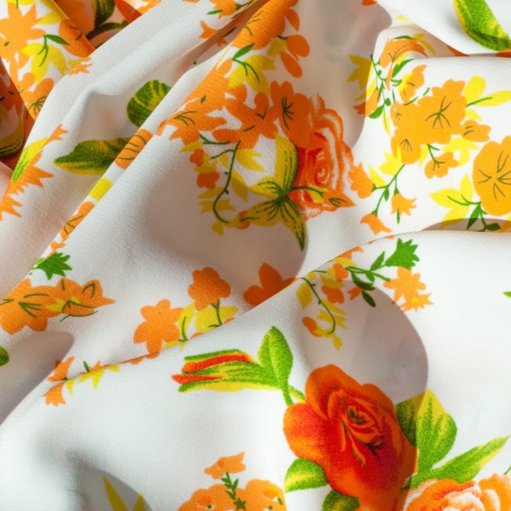 Close-up of bright floral lawn cotton fabric with orange, yellow, and green blooms on a white background.