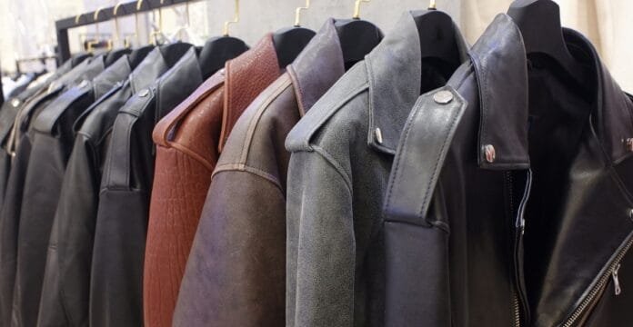 A row of leather coats in various dark colors hanging on a rack, with visible zippers and stitching