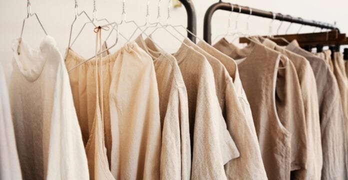 “A row of light, neutral-toned linen garments hanging on a metal clothing rack.”