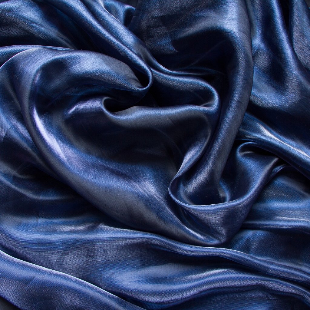 Close-up of rich blue matte organza fabric with soft folds and subtle sheen, showing smooth, slightly crinkled texture and gentle highlights.