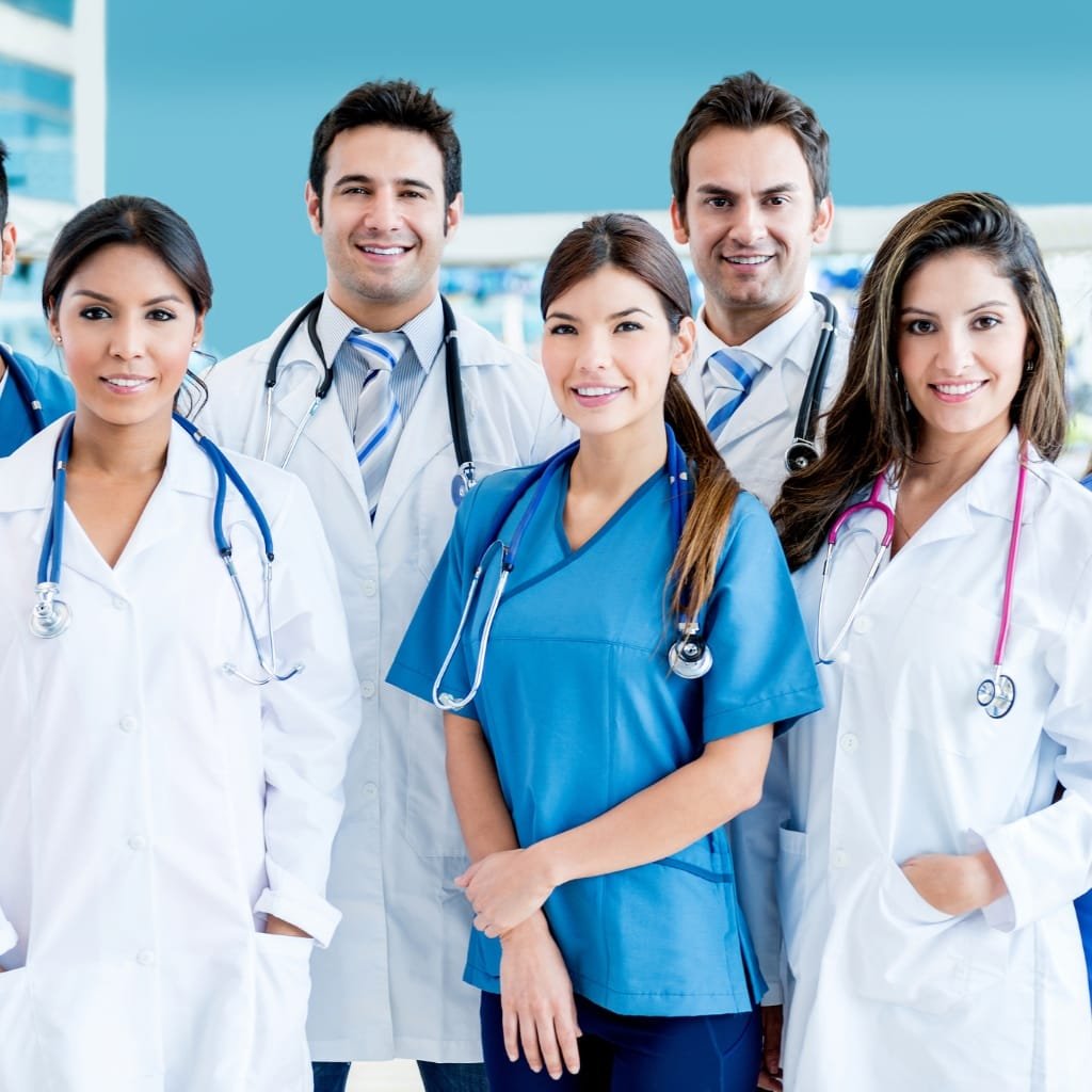 Group of diverse medical professionals in white coats and scrubs, smiling in a bright clinical setting.