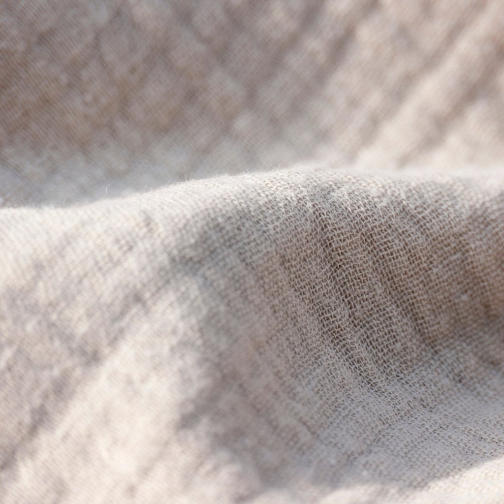 Close-up view of beige linen fabric with soft folds and a textured weave.