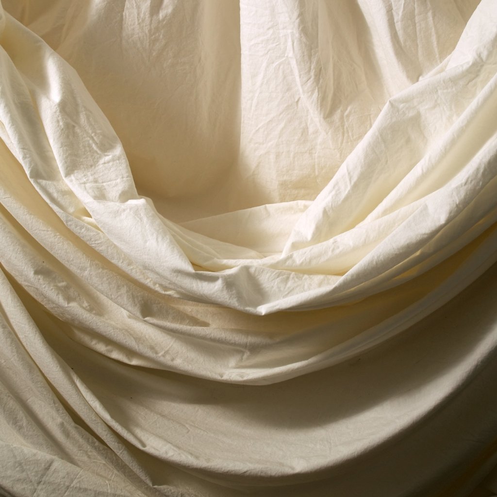 Cream-colored fabric draped and folded in soft, flowing folds, creating gentle shadows and curves.