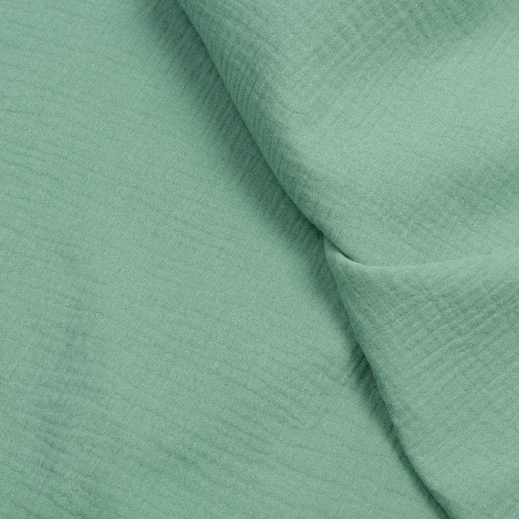 A close-up of soft, light-green muslin cotton fabric with gentle folds and a smooth, breathable texture.