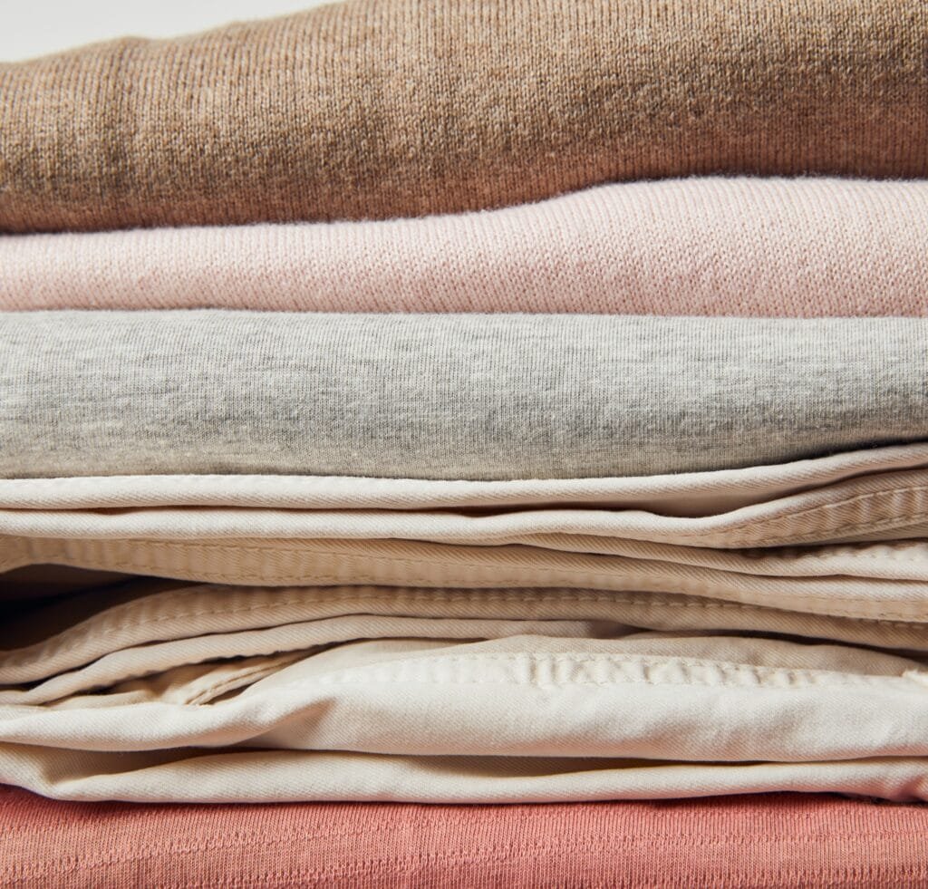 A stacked pile of napped linen fabric in soft, muted colors (beige, pink, gray, and brown) with a slightly fuzzy, brushed finish.