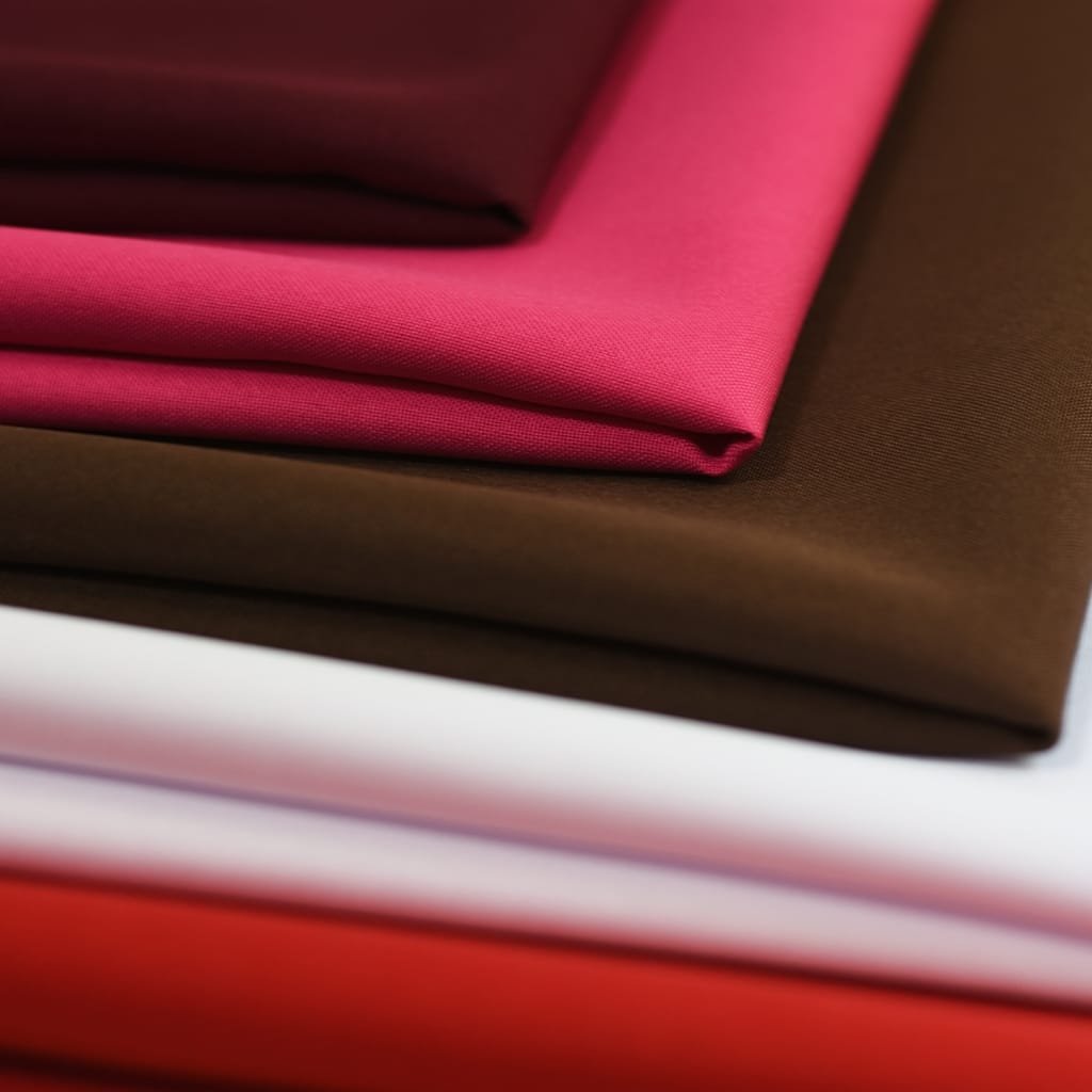 Stack of folded fabrics in magenta, brown, and red tones with soft textures. oxfard cotton fabric