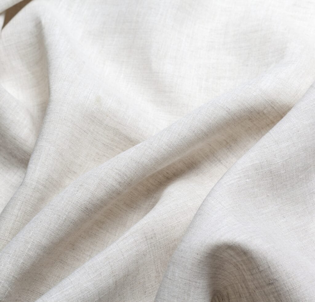 A close-up view of plain linen fabric with soft natural creases and a light, neutral color.
