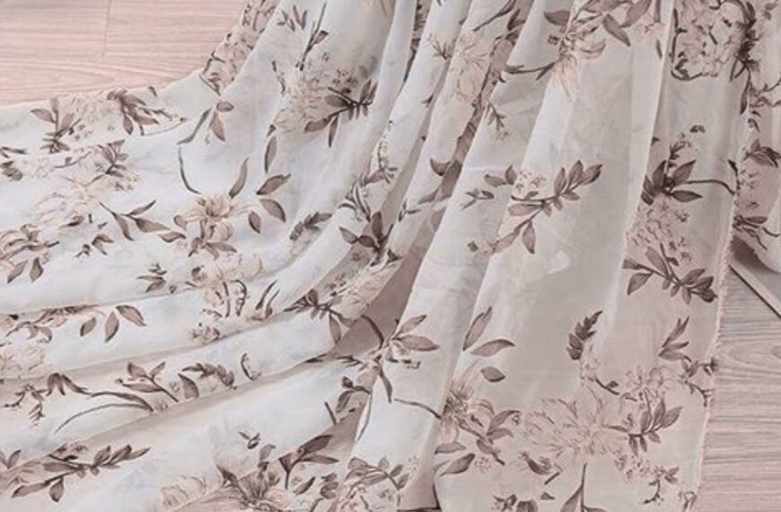 Soft, sheer organza fabric with a delicate floral print in light pink and beige tones draped over a pale wooden floor. Printed Organza Fabric