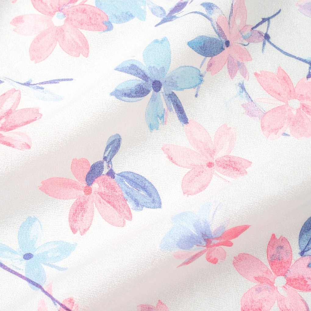 Close-up of lightweight organza fabric with a delicate pink and blue floral print on a pale background.