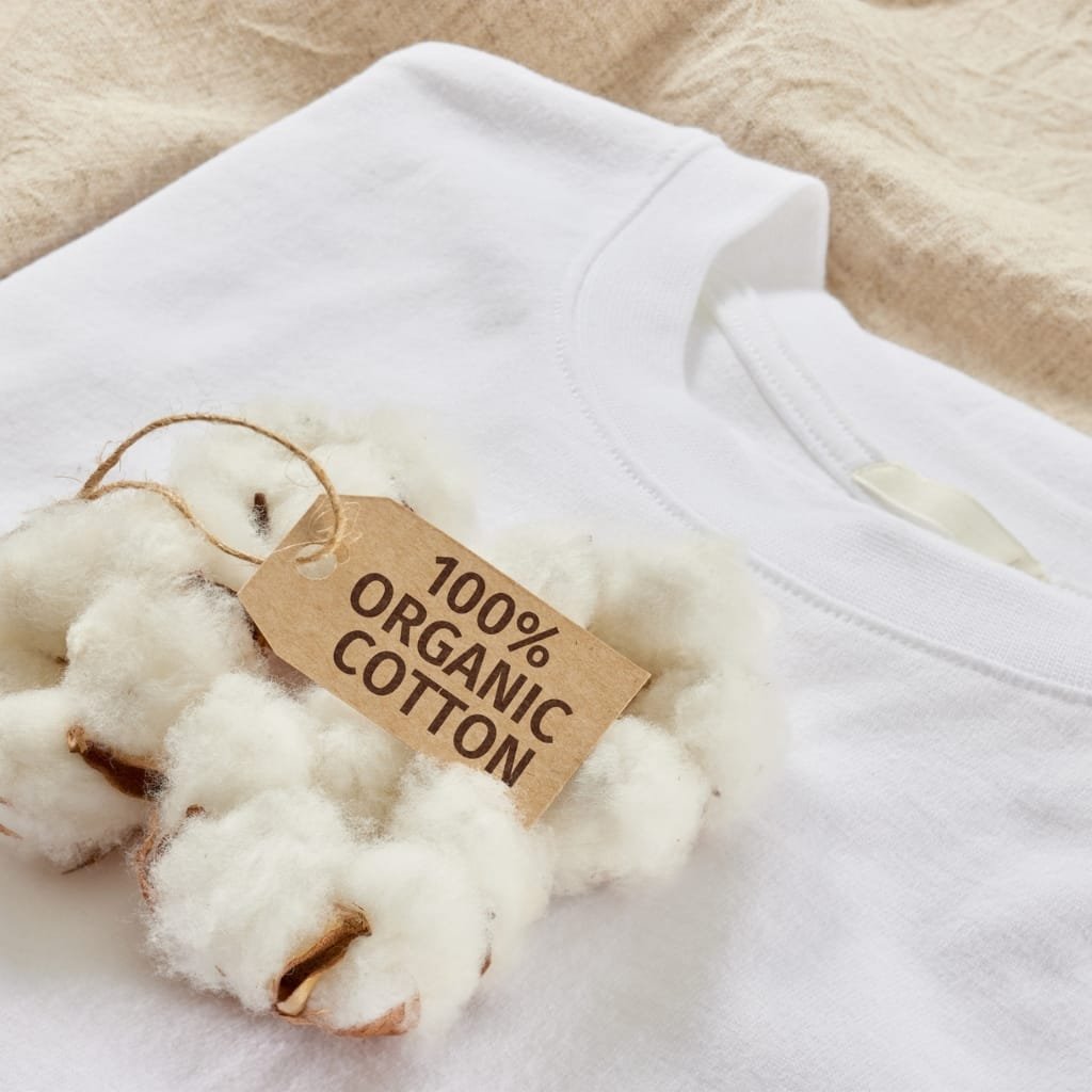 Close-up of a white cotton T-shirt with a tag reading '100% Organic Cotton' and cotton bolls placed on top, highlighting use of upland cotton in products.