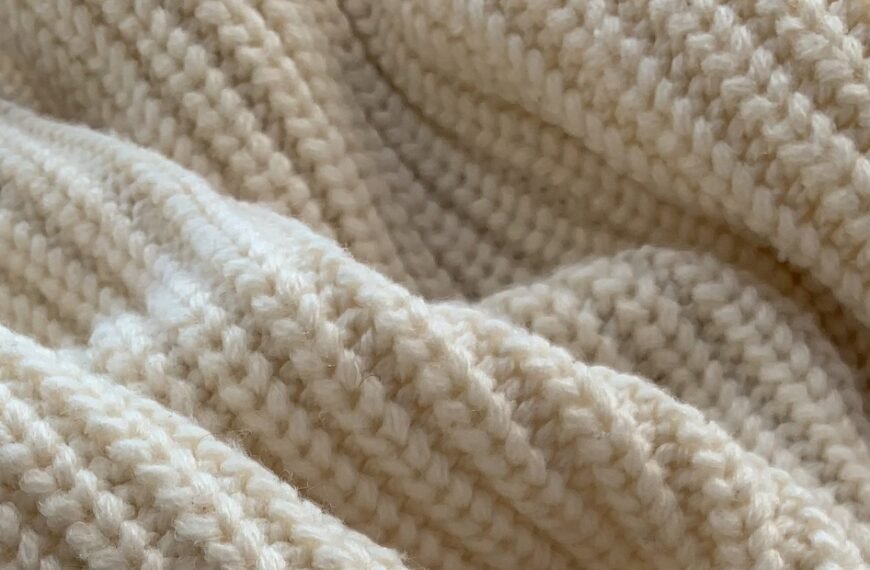 A close-up of creamy, chunky-knit fabric with soft folds and a cozy texture.