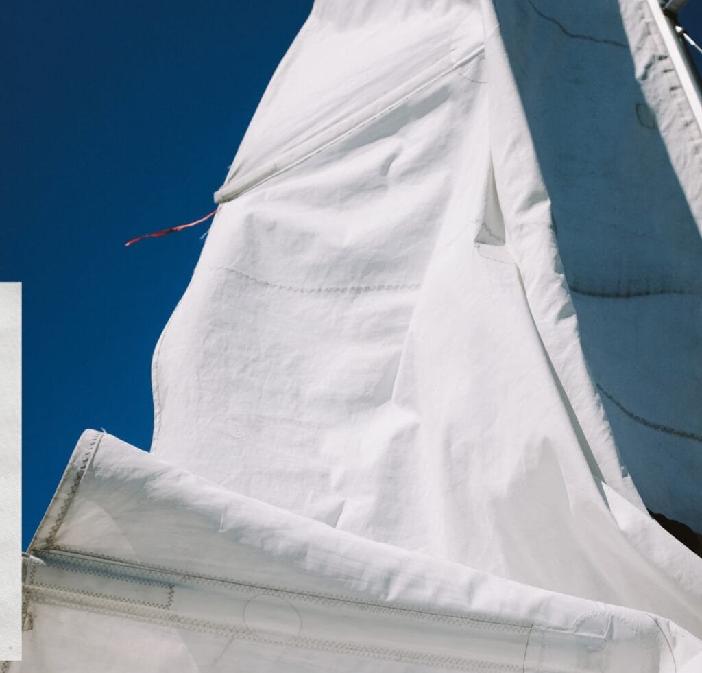 A close-up of white sailcloth fabric with visible stitching, seams, and a small red thread against a deep blue sky. 23 Types of Linen Fabric