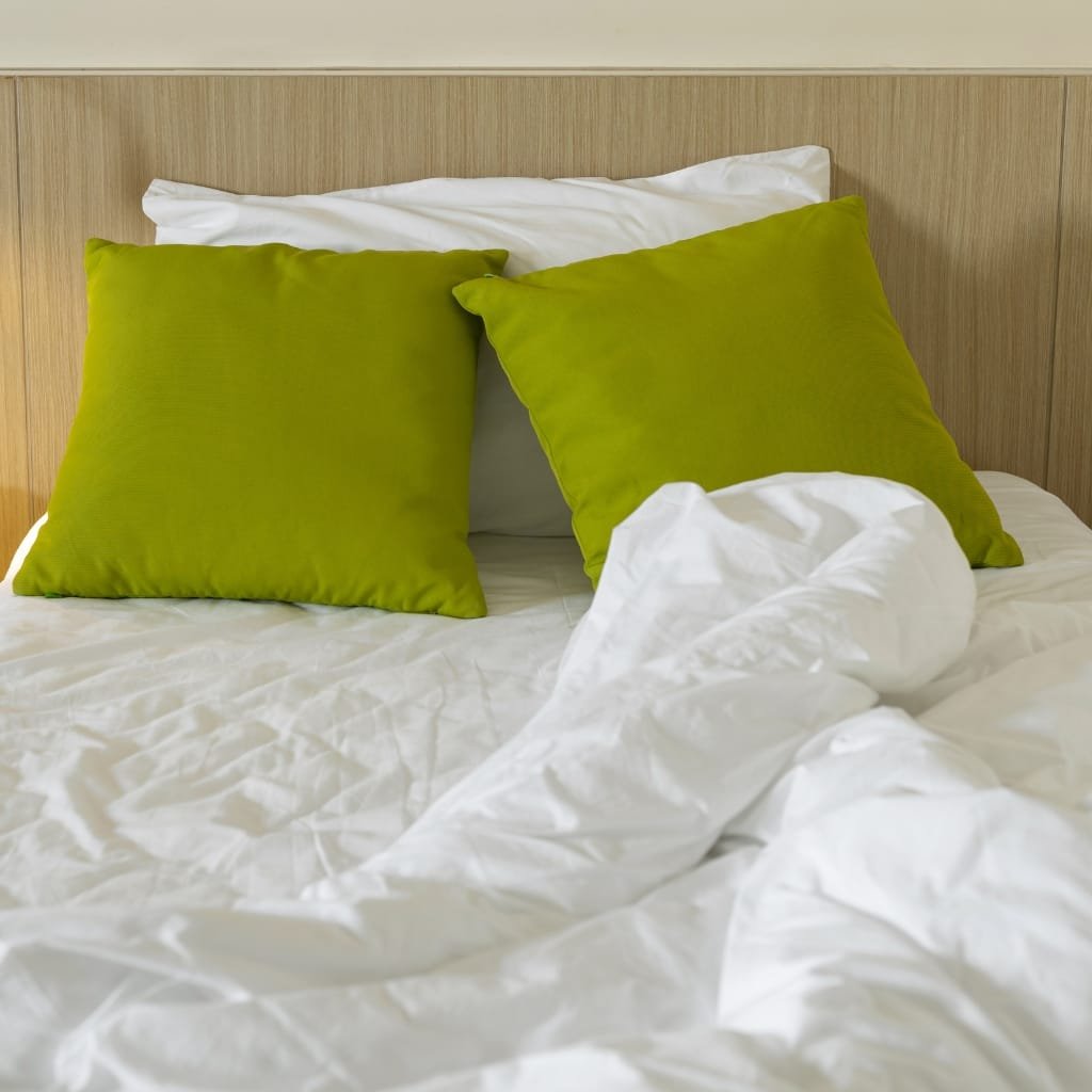 "A neatly made bed with two bright green pillows against a light wood headboard and white rumpled duvet in the foreground. sateen cotton fabric