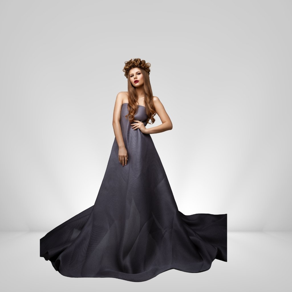 A elegant woman wearing a flowing satin organza evening gown in a dark charcoal shade, standing against a light gray studio backdrop with a long voluminous train.