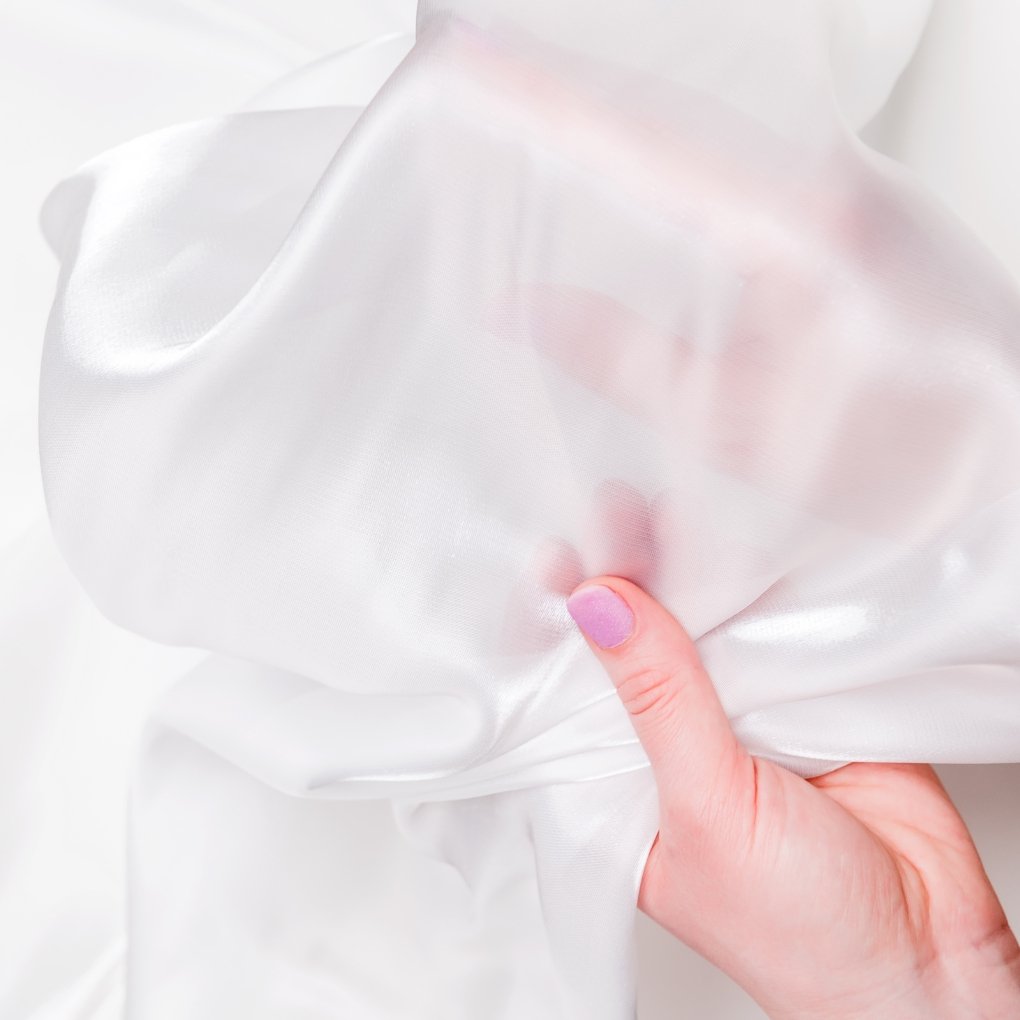 Close-up of a hand pinching soft, sheer organza fabric, showing a translucent, delicate weave and gentle folds.
