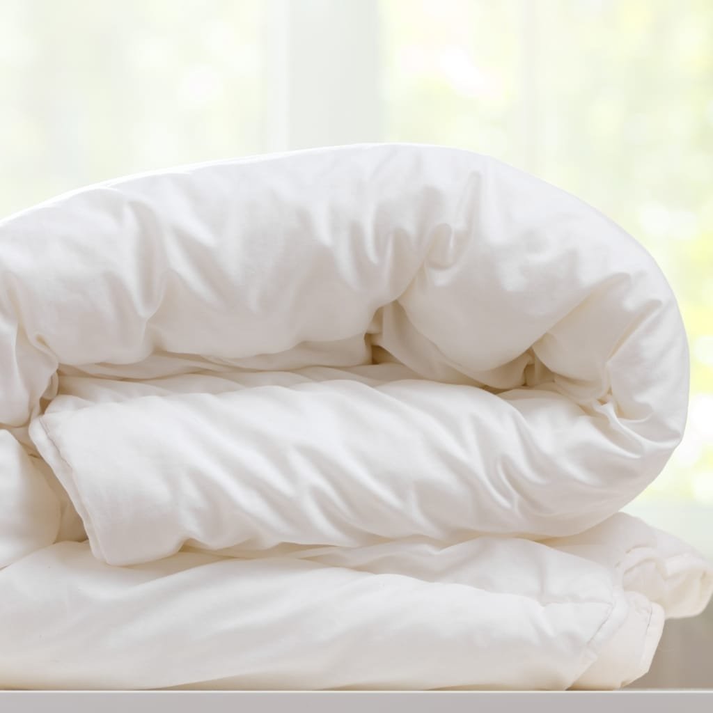 Close-up of a white, fluffy folded duvet or comforter on a light surface, highlighting soft cotton fabric and cozy folds.