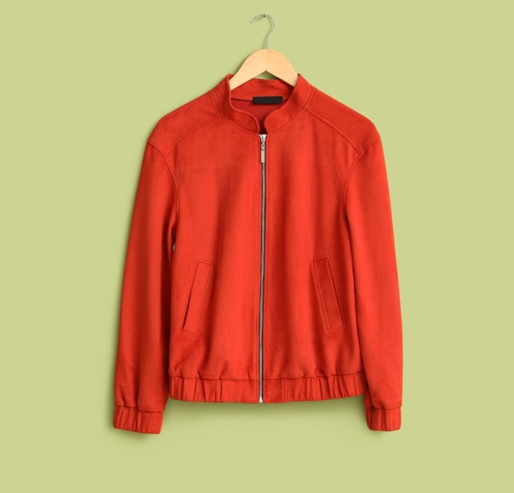 "Red slim-fit bomber jacket hanging on a wooden hanger against a pale olive-green background, full-front view with zipper closure and two side pockets.
