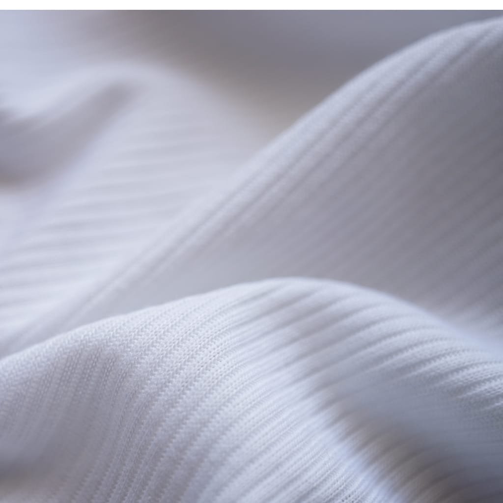 A close-up of soft, white fabric with subtle ribbed texture and gentle folds.