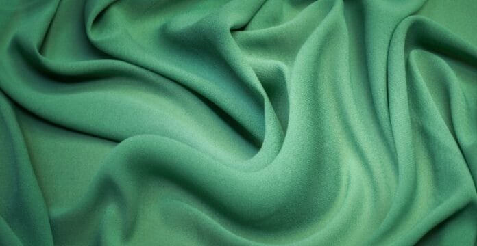 A close-up of smooth, flowing emerald-green fabric with soft folds and a velvety texture.