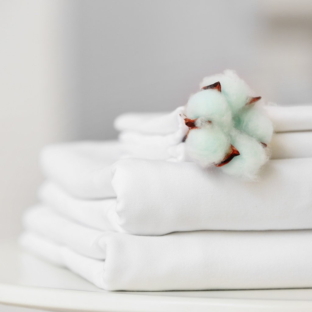 Why Supima Cotton Feels Softer, Stronger, and Smarter 21 Stack of neatly folded white towels with a cotton plant fiber decoration on top.