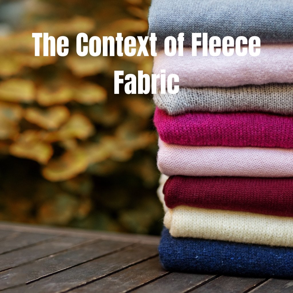 Stack of folded fleece fabric in varying colors (gray, light gray, pink, magenta, cream, burgundy, navy) on a wooden surface with autumn blurred leaves in the background.