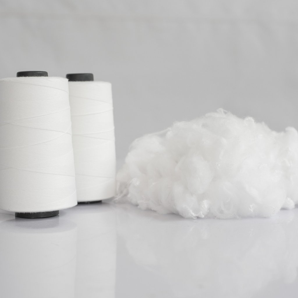 Two white thread spools and a fluffy white fiber on a pale background.