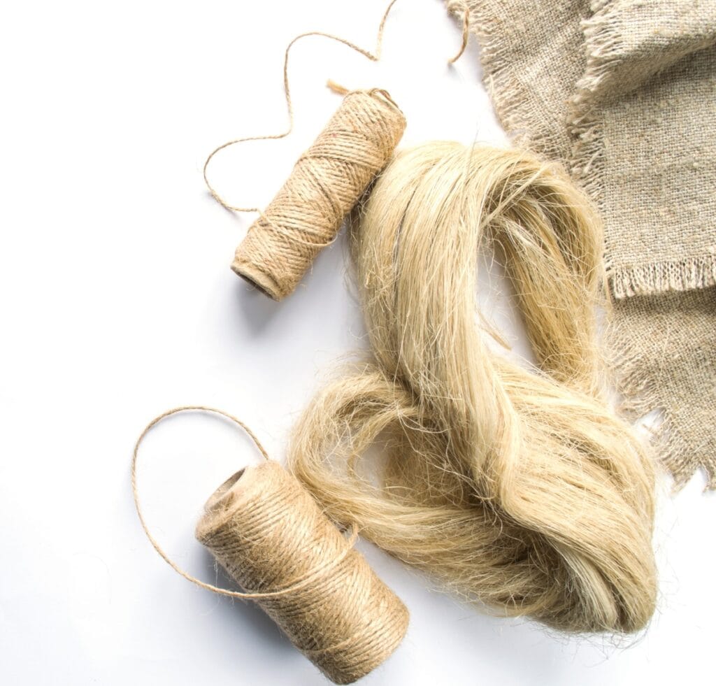 A skein of golden-beige linen fiber and two small spools of twine, with rough woven linen fabric pieces in the background.