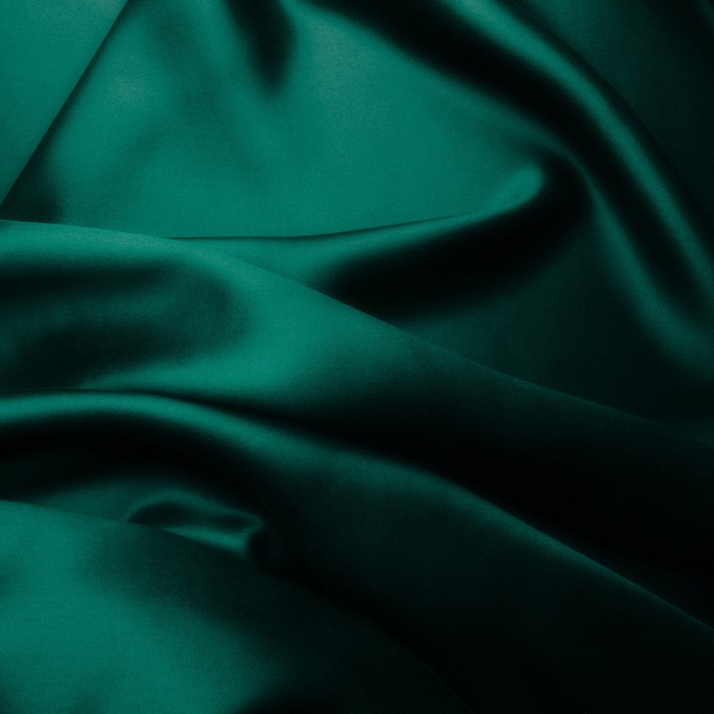 A close-up photograph of rich, emerald satin organza fabric with smooth, flowing folds and subtle sheen.