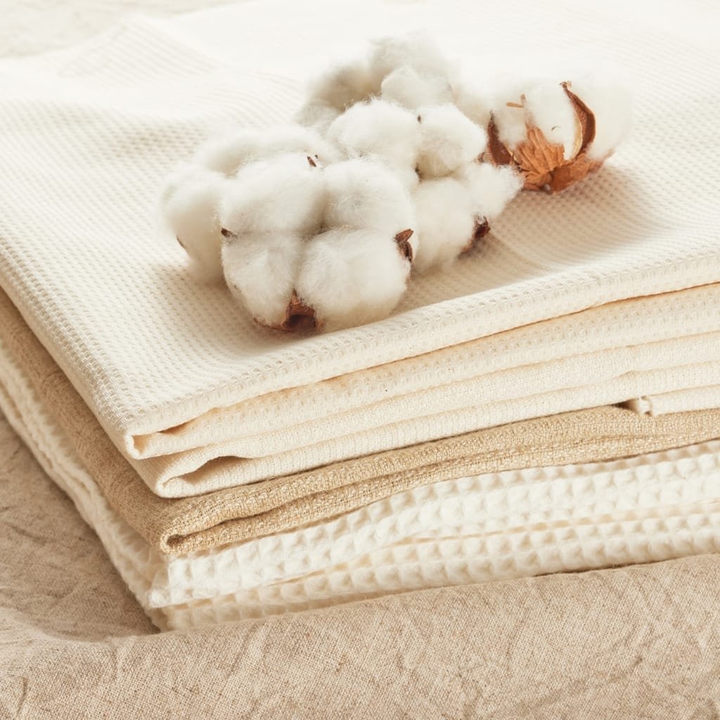 Stack of neatly folded beige and cream cotton fabric with a fluffy cotton boll resting on top, conveying soft, natural texture.